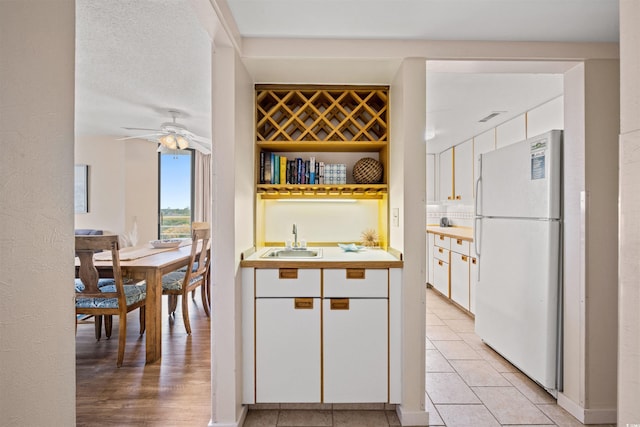 kitchen featuring white cabinets, ceiling fan, white refrigerator, and sink