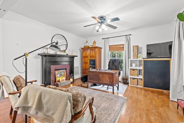 office space featuring a brick fireplace, light hardwood / wood-style flooring, ornamental molding, and ceiling fan