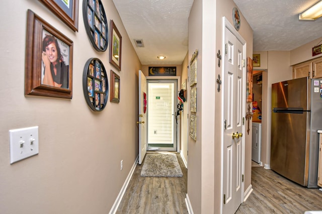 hall featuring light wood-type flooring, a textured ceiling, and washer / clothes dryer