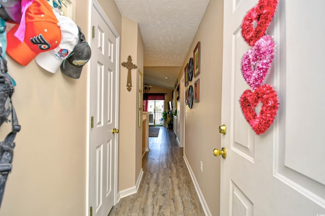 hall with hardwood / wood-style flooring, a textured ceiling, and vaulted ceiling