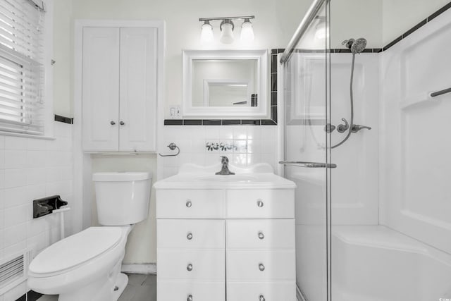 bathroom with tile walls, an enclosed shower, vanity, and toilet