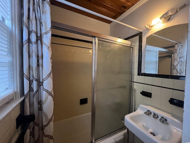 bathroom featuring bath / shower combo with glass door, tile walls, crown molding, and a sink