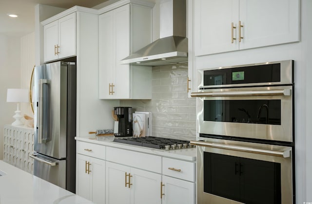 kitchen with appliances with stainless steel finishes, tasteful backsplash, white cabinetry, and wall chimney exhaust hood