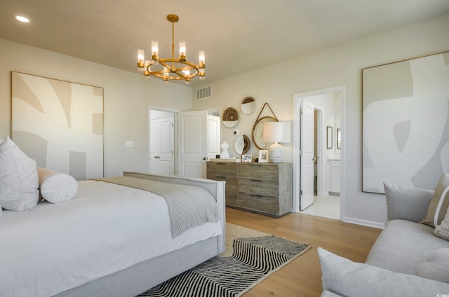 bedroom featuring a notable chandelier, light wood-type flooring, and ensuite bath