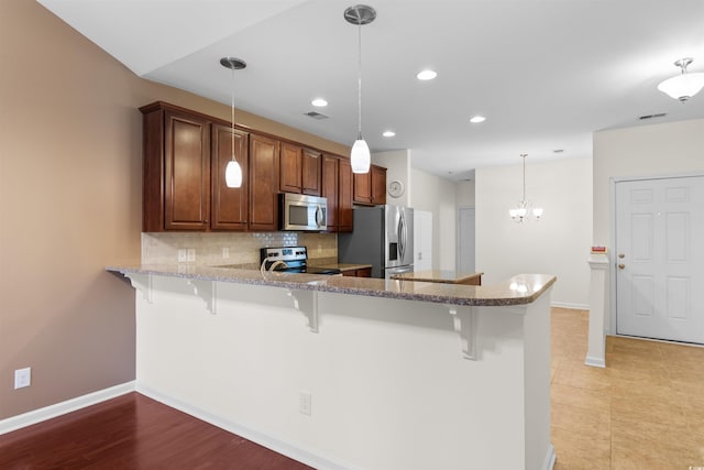 kitchen featuring a kitchen breakfast bar, kitchen peninsula, hanging light fixtures, and appliances with stainless steel finishes