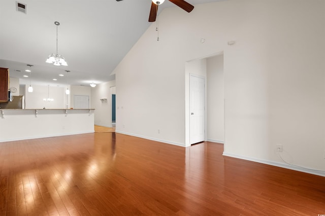 unfurnished living room featuring ceiling fan with notable chandelier, high vaulted ceiling, and hardwood / wood-style flooring