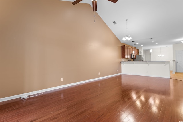 unfurnished living room with hardwood / wood-style floors, ceiling fan with notable chandelier, and high vaulted ceiling