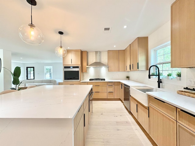 kitchen with light hardwood / wood-style floors, a center island, wall chimney exhaust hood, light brown cabinets, and appliances with stainless steel finishes