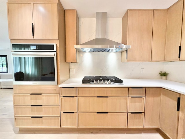 kitchen with light brown cabinets, appliances with stainless steel finishes, decorative backsplash, and wall chimney exhaust hood