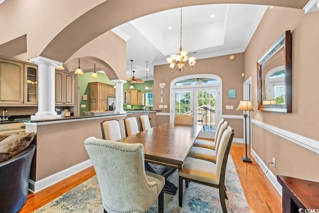 dining room featuring an inviting chandelier, sink, crown molding, light wood-type flooring, and a tray ceiling