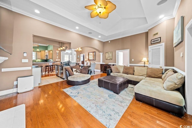 living room featuring a tray ceiling, crown molding, wood-type flooring, and ceiling fan with notable chandelier