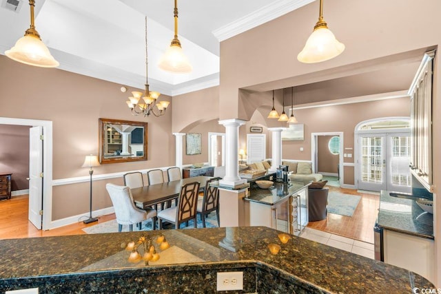 kitchen with ornate columns, crown molding, dark stone counters, pendant lighting, and light hardwood / wood-style floors