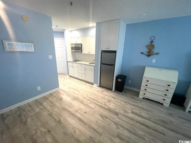 kitchen with backsplash, white cabinetry, stainless steel appliances, and light wood-type flooring