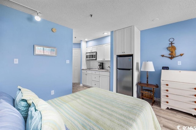 bedroom featuring stainless steel fridge, light hardwood / wood-style floors, a textured ceiling, and a closet