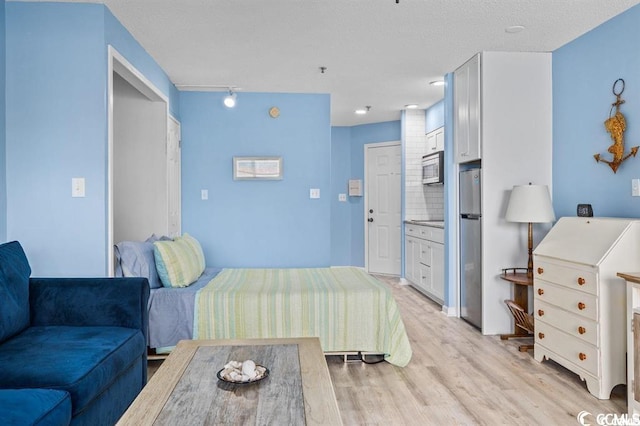 bedroom with light wood-type flooring, ensuite bathroom, and stainless steel refrigerator