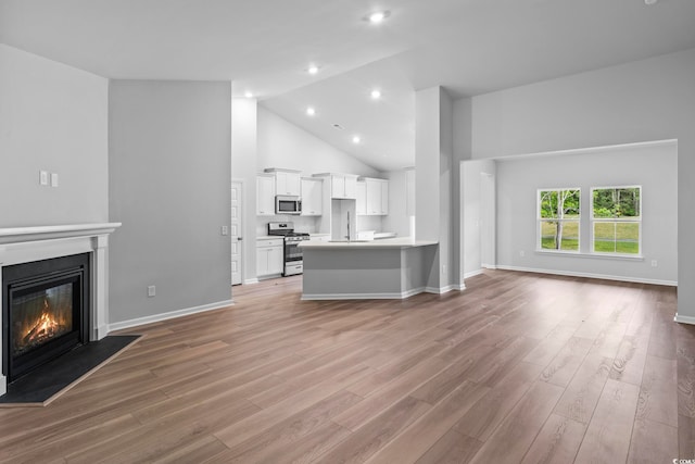 9746 Indigo Creek Blvd, Murrells Inlet, SC 29576 - unfurnished living room with light wood-style flooring, a glass covered fireplace, high vaulted ceiling, baseboards, and recessed lighting