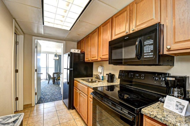 kitchen with black appliances, light stone counters, a paneled ceiling, light tile patterned floors, and sink