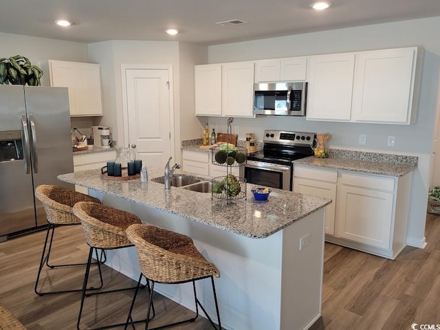 kitchen with stainless steel appliances, light hardwood / wood-style floors, a center island with sink, a breakfast bar, and white cabinets