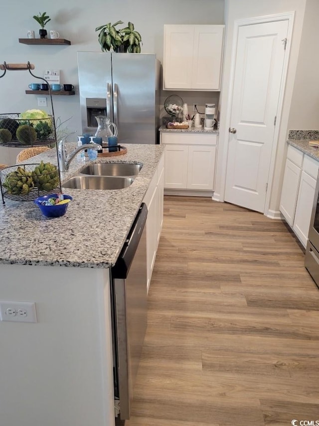 kitchen with light stone counters, stainless steel appliances, sink, white cabinets, and light hardwood / wood-style flooring