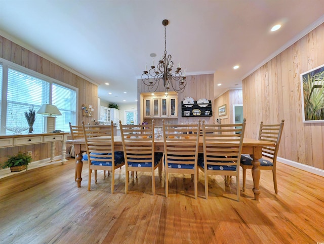 dining space with light hardwood / wood-style floors, a chandelier, wooden walls, and ornamental molding