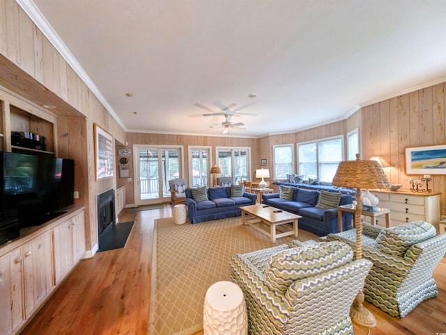 living room featuring ornamental molding, hardwood / wood-style floors, wood walls, and ceiling fan