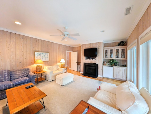 living room with wood walls, light hardwood / wood-style floors, ceiling fan, and ornamental molding