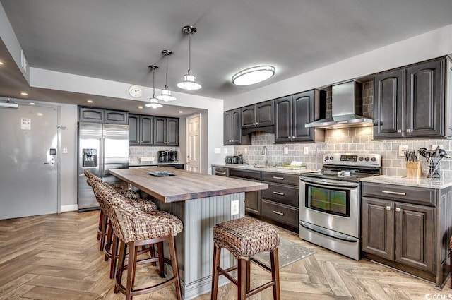 kitchen featuring appliances with stainless steel finishes, wall chimney exhaust hood, light parquet floors, and wood counters