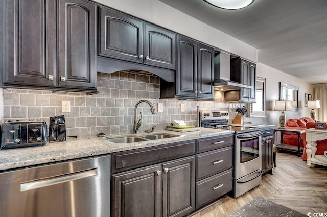 kitchen with light stone counters, appliances with stainless steel finishes, sink, and wall chimney exhaust hood