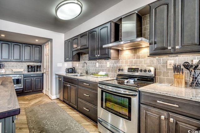 kitchen with light stone counters, sink, tasteful backsplash, wall chimney range hood, and appliances with stainless steel finishes