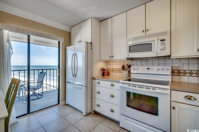 kitchen with white appliances, a water view, a textured ceiling, light tile patterned flooring, and decorative backsplash