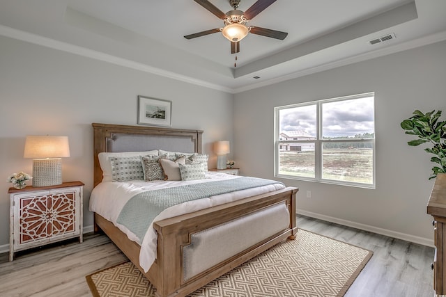 bedroom with light wood-type flooring, a tray ceiling, ceiling fan, and crown molding