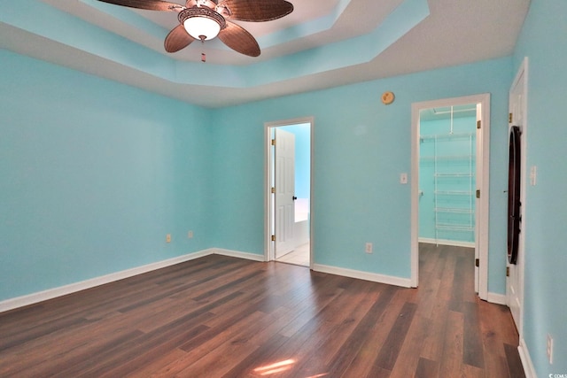 unfurnished bedroom featuring a closet, a spacious closet, dark hardwood / wood-style floors, ceiling fan, and a raised ceiling