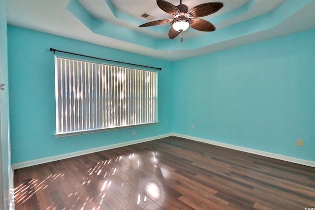 spare room featuring dark wood-type flooring, ceiling fan, and a raised ceiling