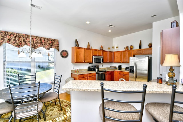 kitchen with stainless steel appliances, kitchen peninsula, a kitchen breakfast bar, decorative light fixtures, and light hardwood / wood-style flooring