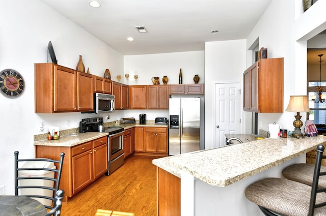 kitchen featuring kitchen peninsula, stainless steel appliances, light hardwood / wood-style floors, and a breakfast bar