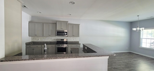 kitchen with stainless steel appliances, tasteful backsplash, an inviting chandelier, gray cabinets, and dark hardwood / wood-style flooring