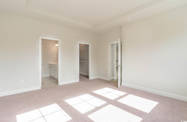 unfurnished bedroom featuring light carpet, a walk in closet, a closet, and ensuite bathroom