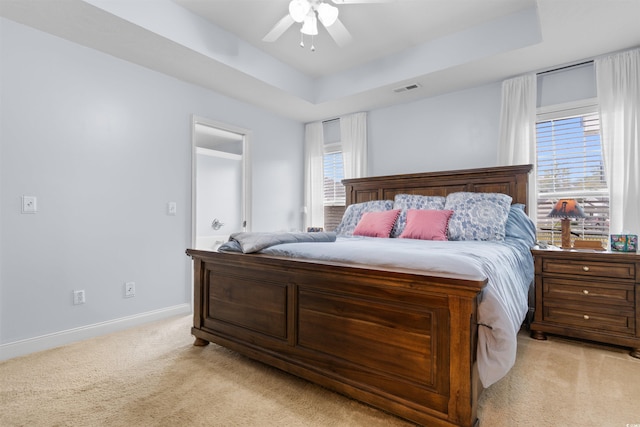 bedroom featuring ceiling fan, a tray ceiling, multiple windows, and light colored carpet