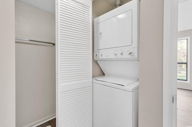 clothes washing area with wood-type flooring, a textured ceiling, and stacked washer and clothes dryer