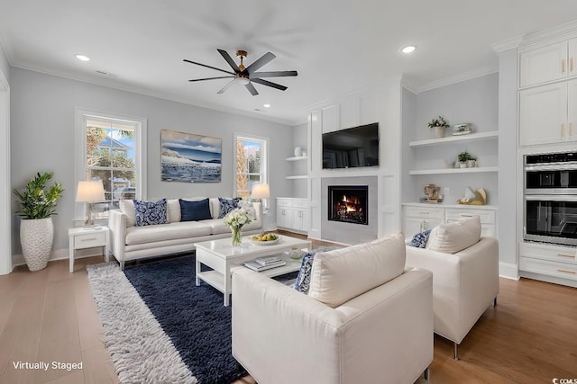 living room featuring hardwood / wood-style flooring, built in shelves, ceiling fan, and crown molding