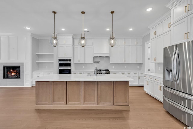 kitchen with white cabinets, appliances with stainless steel finishes, decorative light fixtures, and an island with sink