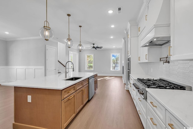 kitchen with premium range hood, white cabinets, sink, an island with sink, and light hardwood / wood-style floors