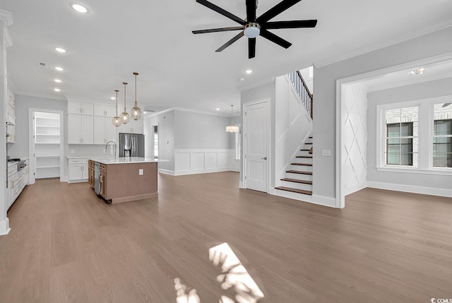 kitchen with hanging light fixtures, light hardwood / wood-style flooring, stainless steel refrigerator with ice dispenser, a large island with sink, and white cabinets