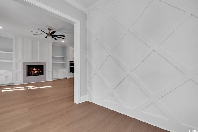 unfurnished living room featuring ceiling fan, built in features, ornamental molding, and light hardwood / wood-style flooring