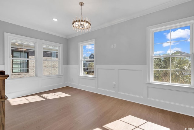 unfurnished dining area featuring crown molding, plenty of natural light, an inviting chandelier, and hardwood / wood-style flooring