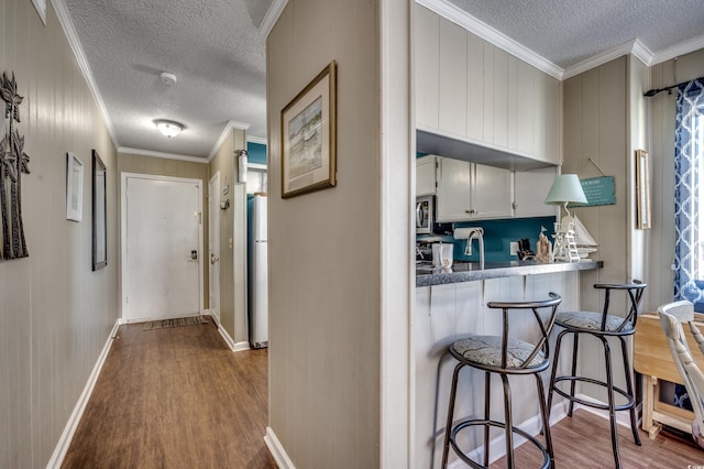 hallway with ornamental molding, a textured ceiling, and light wood-type flooring