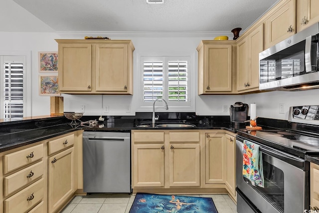 kitchen featuring crown molding, sink, dark stone countertops, light tile patterned floors, and stainless steel appliances