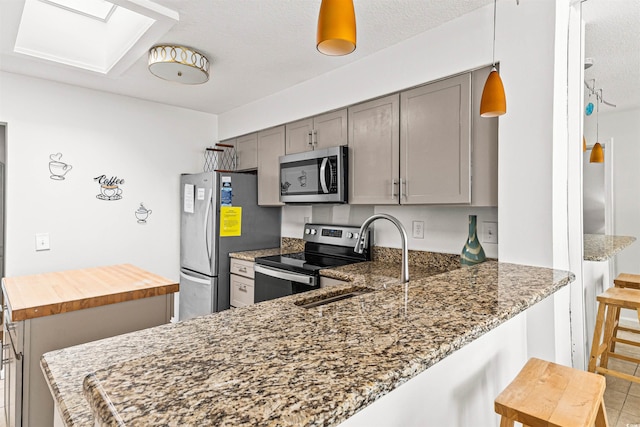 kitchen with dark stone countertops, a skylight, kitchen peninsula, and stainless steel appliances