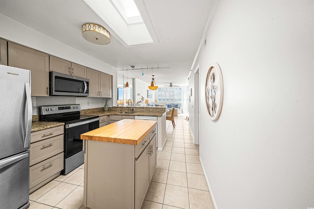 kitchen with sink, appliances with stainless steel finishes, decorative light fixtures, a kitchen island, and butcher block counters