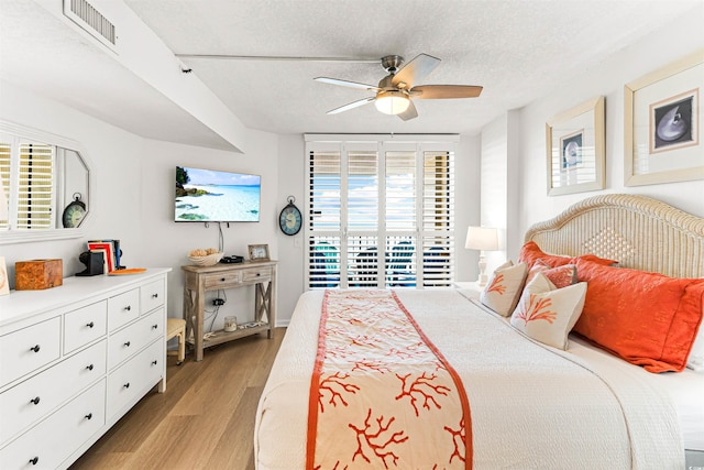 bedroom with a textured ceiling, ceiling fan, light hardwood / wood-style flooring, and multiple windows